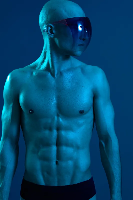 Athletic man with sunglasses showcasing a strong physique, illuminated by a striking blue light, emphasizing confidence and strength in a vibrant atmosphere.