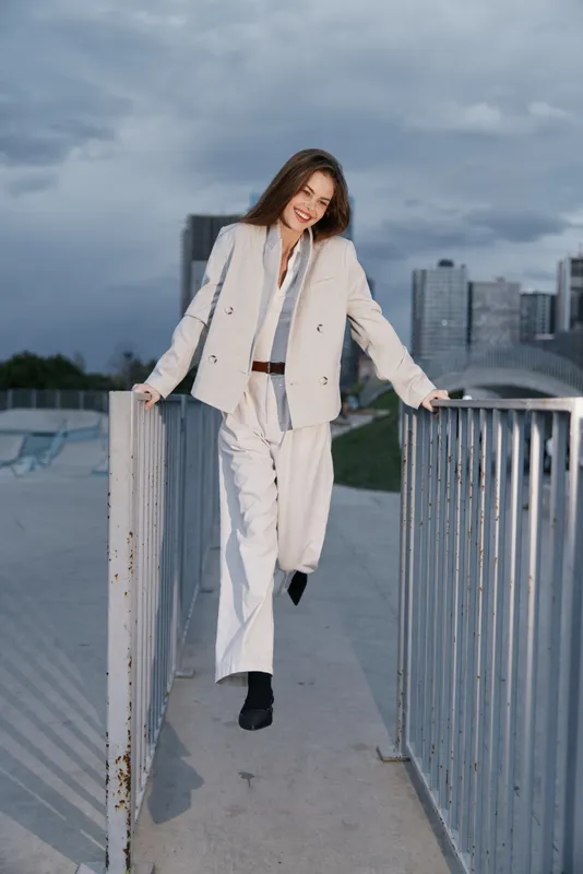 Confident woman in stylish business attire smiling outdoors against an urban skyline backdrop, showcasing professional confidence and modern fashion.