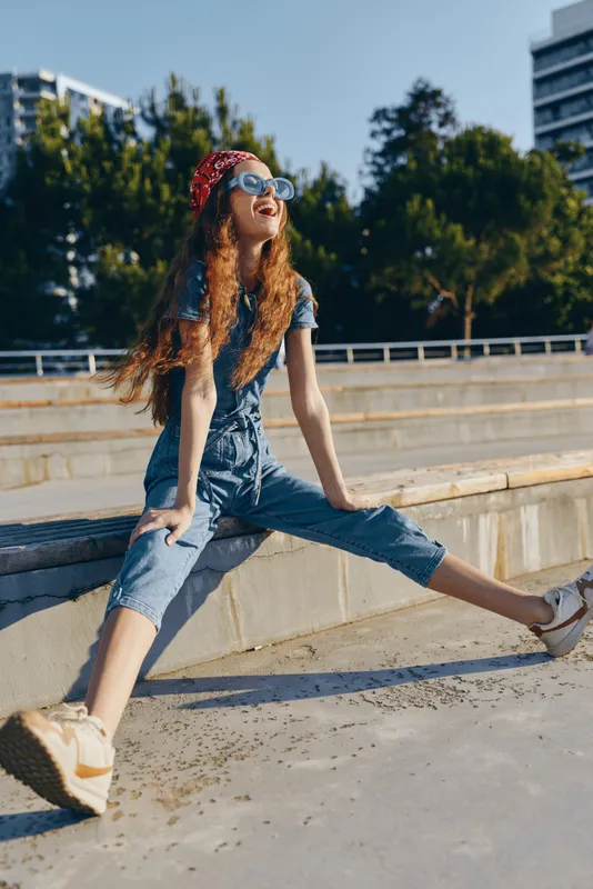 Lifestyle woman in modern boho-western denim street style with curly hair wearing sunglasses and bandana smiling outdoors in warm film color tones.
