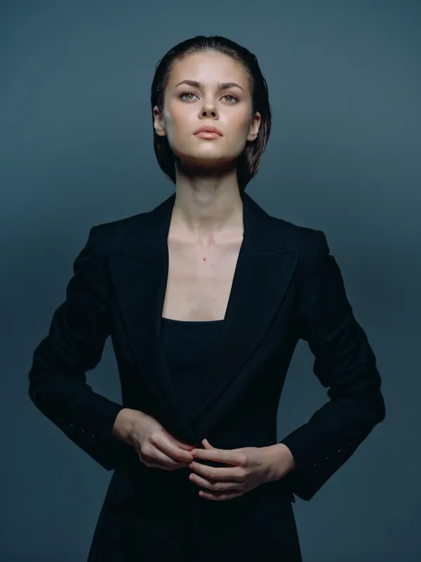 confident woman in black blazer with serious expression on gray background