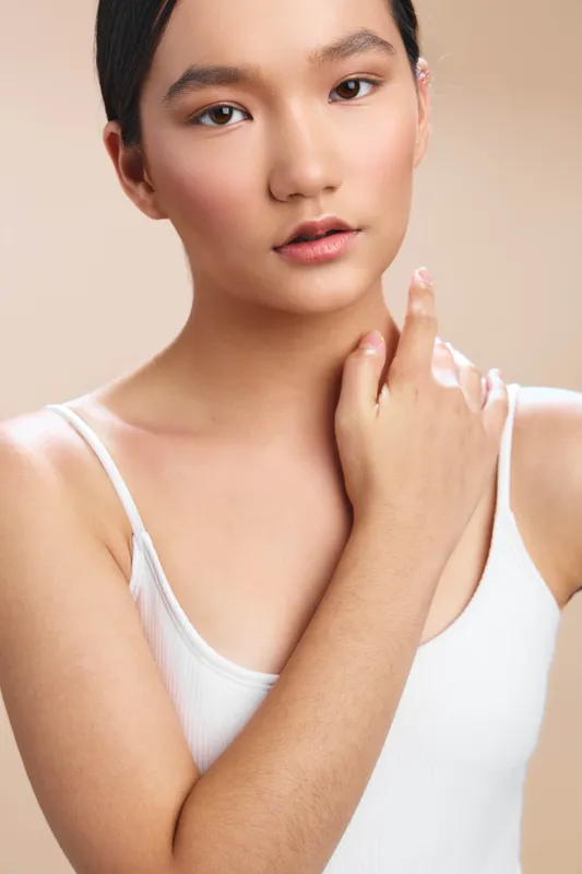asian woman wearing a white tank top stands against a soft neutral backdrop, exuding calm confidence with a gentle expression, suitable for beauty, fashion, and lifestyle campaigns.