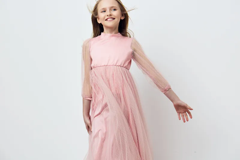 Elegant young girl in a pink dress smiling joyfully against a soft pastel background, capturing a sense of innocence and joy