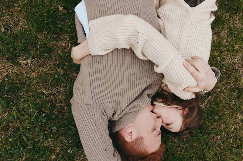 Young couple lying on the grass embraces tenderly with closed eyes enjoying a peaceful moment together in cozy knitted sweaters outdoors in a natural lifestyle setting