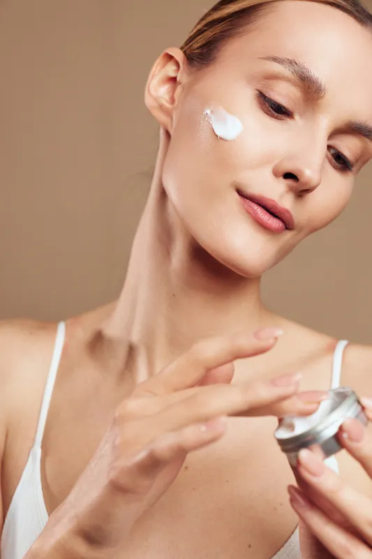 A woman applies cream to her face in a simple skincare routine, emphasizing selfcare and daily beauty rituals in a soft, closeup shot.