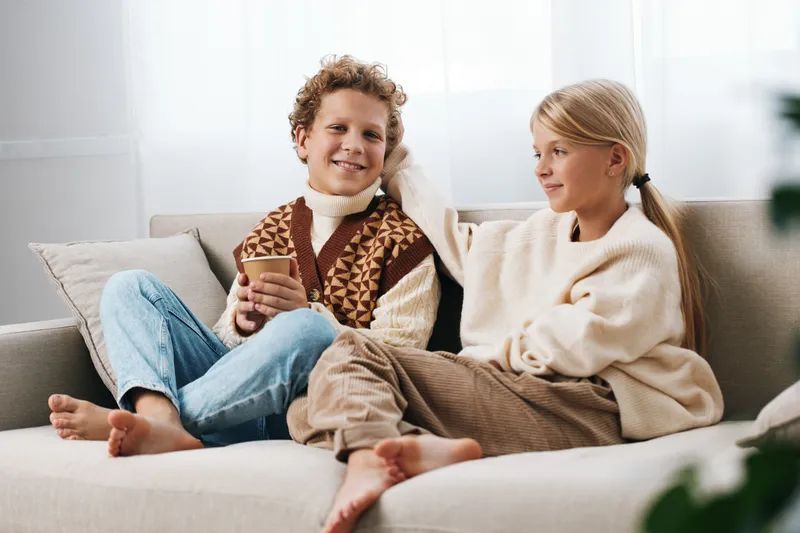 Authentic scene of children at home enjoying a playful moment, capturing a cozy lifestyle with simple school cues, relaxed clothes, and genuine interaction on a sofa.