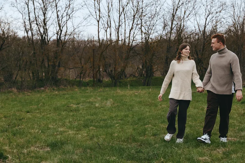 A couple walks hand in hand across a green field, enjoying a calm outdoor moment in a nature rich setting. This lifestyle scene captures love, togetherness, leisure, and simple joy in a bright rural