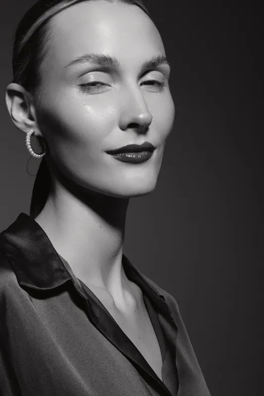 Closeup portrait of a fair skinned Caucasian woman with slicked hair and dark lipstick in studio lighting.