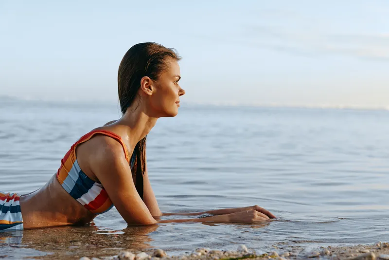 Woman ocean beach sunrise stretching breathing wellness calm, young woman stretches in shallow seawater on a rocky shore, calm ocean waves, soft morning light, concept fitness recovery