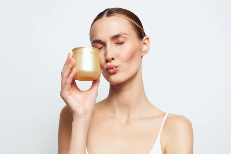 Woman holding jar of cream near face, skincare beauty routine, calm expression, soft light on minimal background, clean wellness spa
