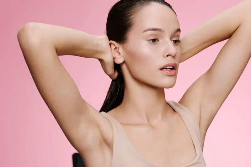 Young woman with neutral expression styling her hair against a pink background, embodying beauty and self care in fashion and lifestyle photography