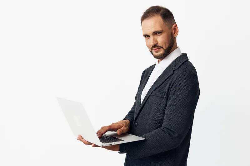 Business professional man stands with a laptop on an isolated white background, radiating confidence, focus, and calm ambition.