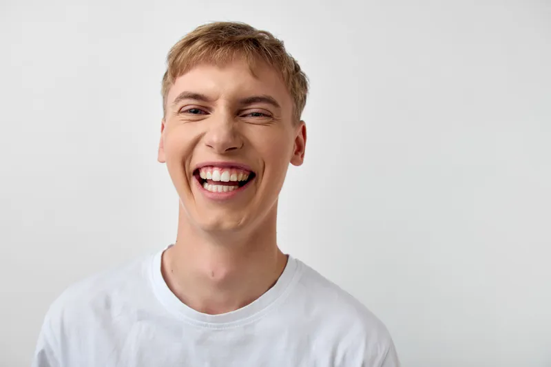 Smiling man in a white shirt, radiating happiness and approachability, bright studio lighting, friendly energy, confident and cheerful expression for branding use