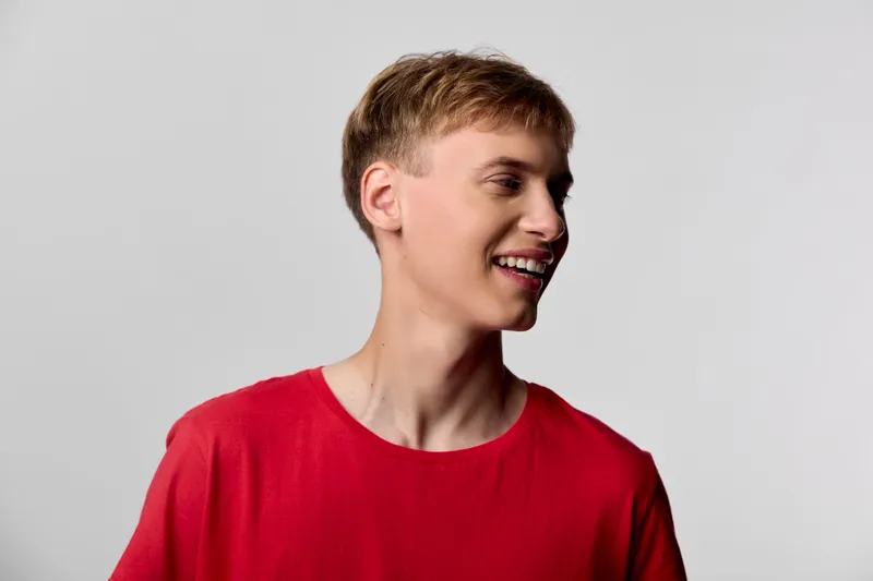 Smiling man in a red shirt stands against a neutral backdrop, a casual headshot capturing a cheerful mood, relaxed posture, and bright studio lighting. Ideal for lifestyle use.