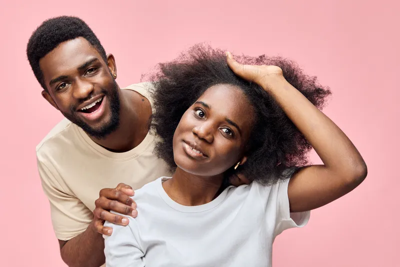 Happy couple with natural hair in casual attire against a pink background, showcasing joy and confidence in a vibrant, colorful lifestyle concept