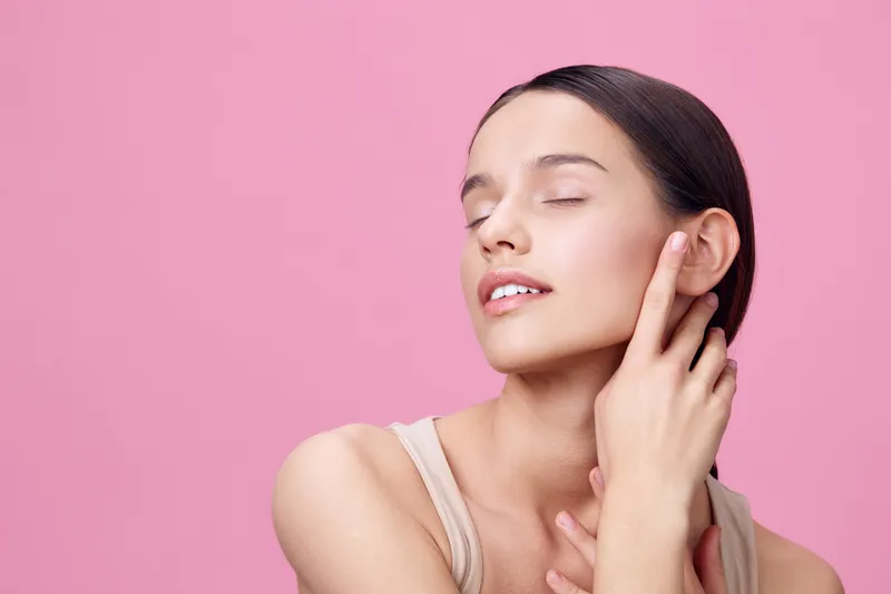 Young woman with fair skin and closed eyes on a pink background, conveying serenity and beauty, ideal for skincare and beauty concepts