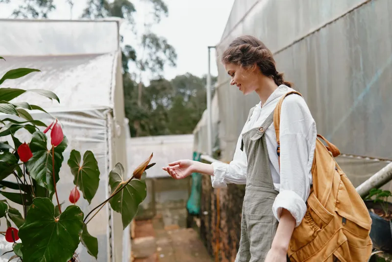 Young woman in casual clothes interacting with plants in a greenhouse, showcasing a sustainable lifestyle and connection to nature