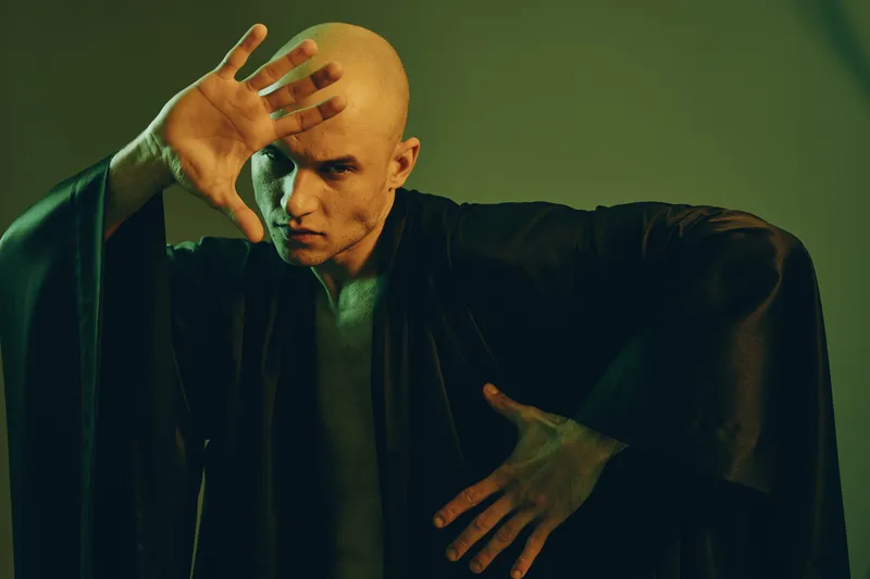 A focused man practicing martial arts in a dark robe, showcasing strength and determination. The dramatic lighting adds an intense atmosphere to this captivating scene.