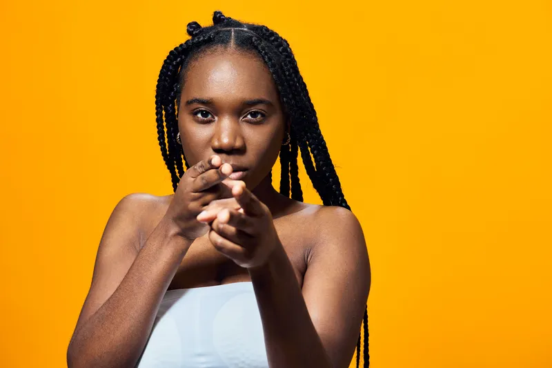 Confident Black woman with braids posing against a vibrant yellow background, wearing a white top, reflecting empowerment and self expression