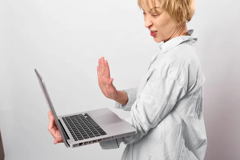 Woman in lab coat holding laptop, raising one hand while speaking, healthcare professional using technology for remote communication, studio background