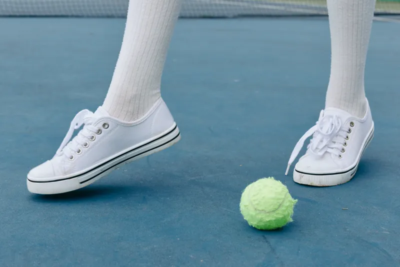 Young athlete in white sneakers and knee high socks playing tennis, focused on the green tennis ball on a blue court
