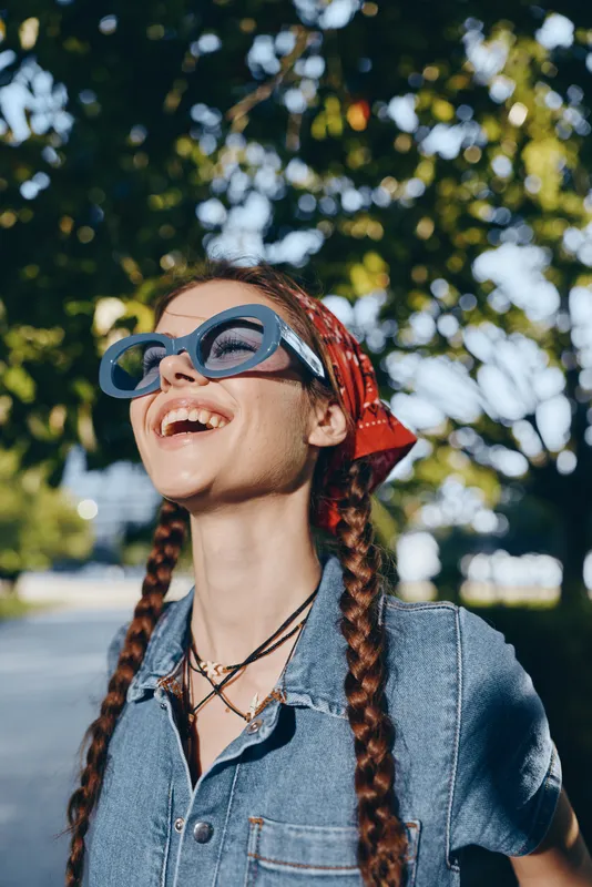 carefree lifestyle woman with modern boho-western denim street style wearing sunglasses and a red bandana, captured in warm film color outdoors under trees
