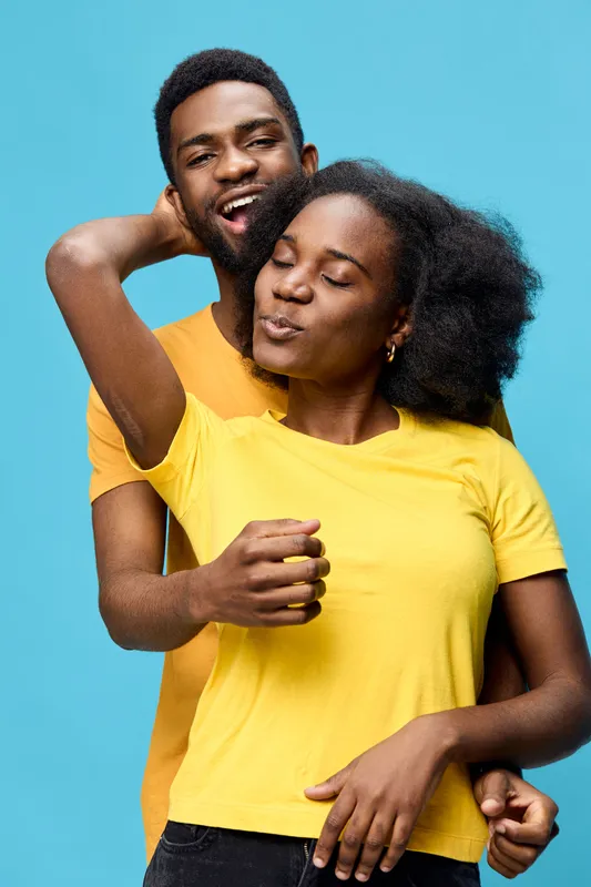Joyful couple embracing against a blue background, wearing bright yellow and orange shirts, depicting love and happiness in a vibrant and cheerful atmosphere