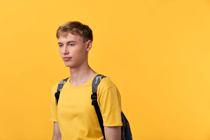 Yellow shirted young man with a backpack stands before a bright yellow backdrop, showcasing casual streetwear, everyday travel vibe and clean composition for lifestyle or e commerce use