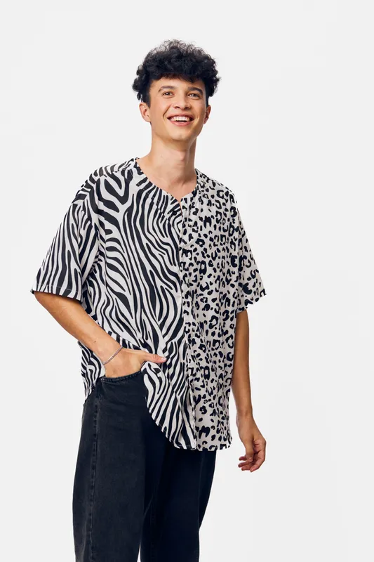 smiling man in casual animal print shirt with black pants, standing against white background, happy young adult expressing positive energy