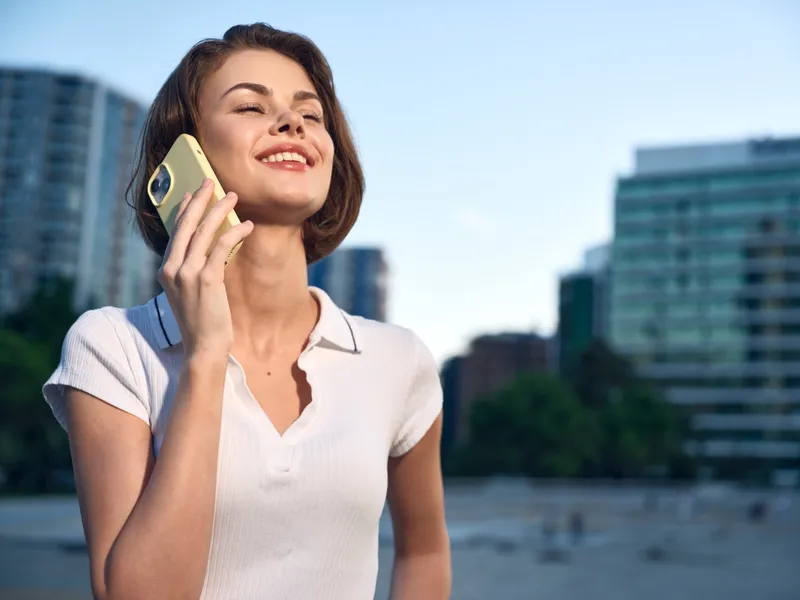 A cheerful woman talks on a mobile phone in a bright urban setting. She smiles confidently, projecting a positive, modern lifestyle and an engaging moment.