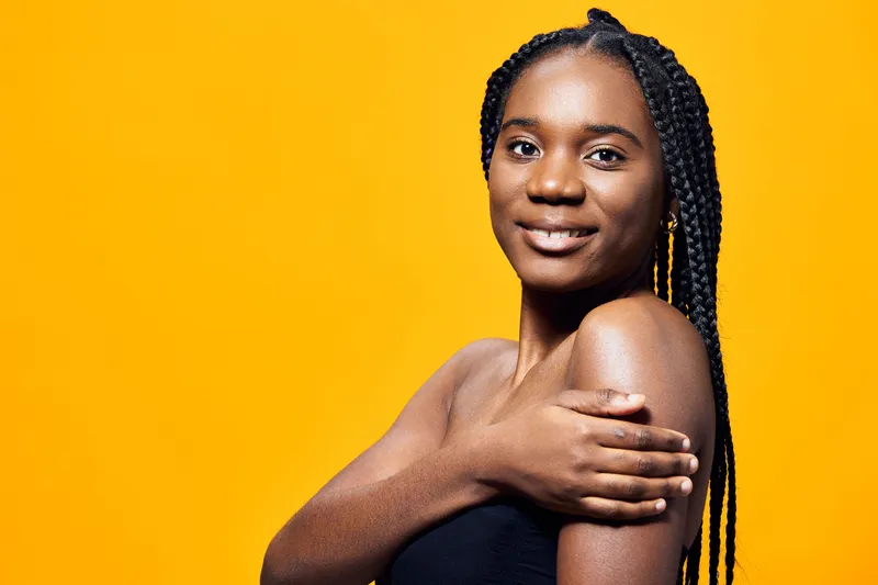 Smiling young black woman with braids against a vibrant yellow background, showcasing beauty and confidence in a stylish, modern setting