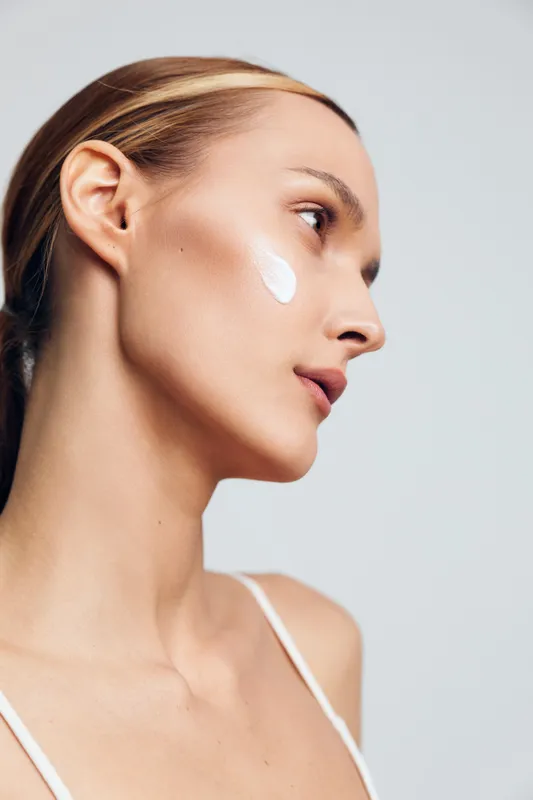 woman skincare face cream beauty hygiene care dermatology routine wellness, side profile young woman applying moisturizer, minimal light background, concept of calm