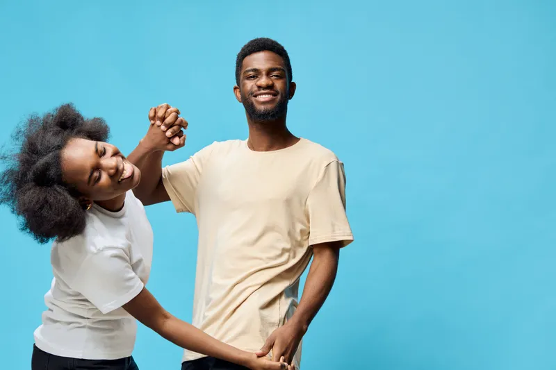 Happy couple enjoying playful interaction against a vibrant blue background, showcasing joy, love, and connection with trendy casual outfits