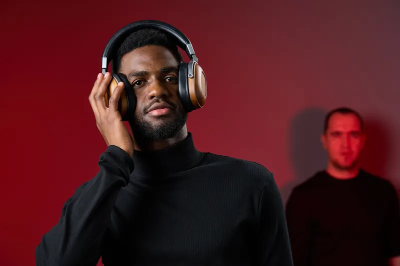 Stylish Black Man Enjoying Music with Headphones Against a Red Background in a Studio Setting