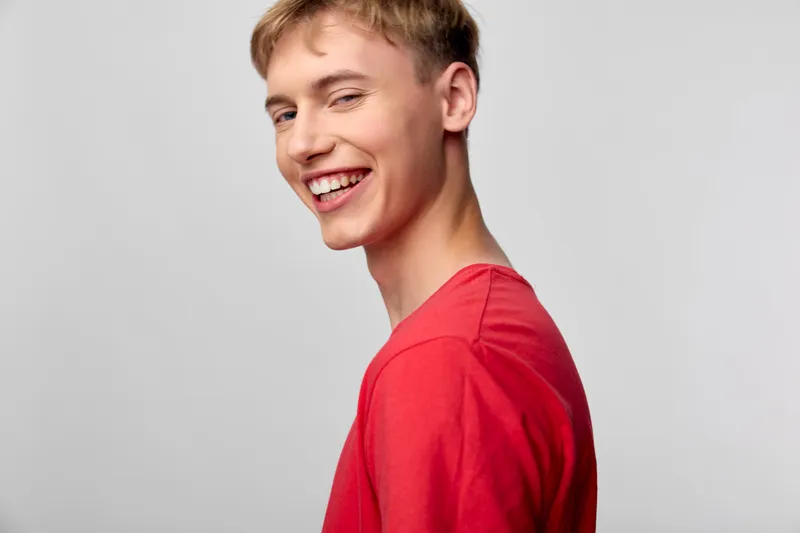 Smiling man in a red shirt in a casual studio setting with bright lighting, conveying approachability, warmth, and friendly mood suitable for lifestyle, fashion, and marketing visuals