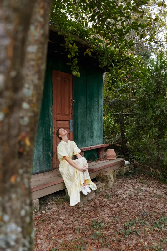 Woman on rustic porch of green cabin in nature peaceful contemplative pose authenticity inclusivity relaxed mood