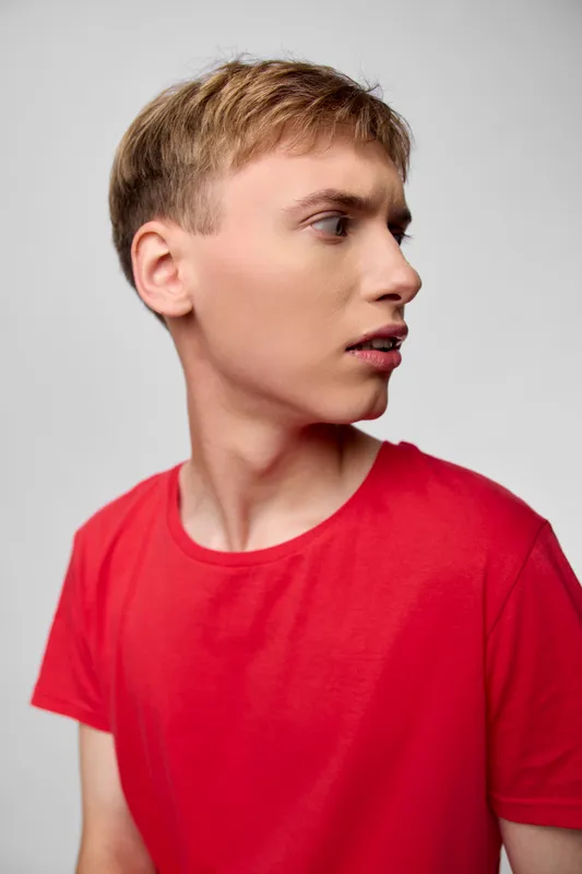 Side profile of a young man in a red shirt against a neutral backdrop, conveying focus, casual style, and modern fashion for stock photography and lifestyle imagery.