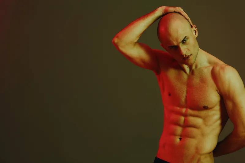 Athletic man posing confidently in a vibrant light setting, showcasing his fit physique and expression of strength. Perfect for fitness and wellness themes.