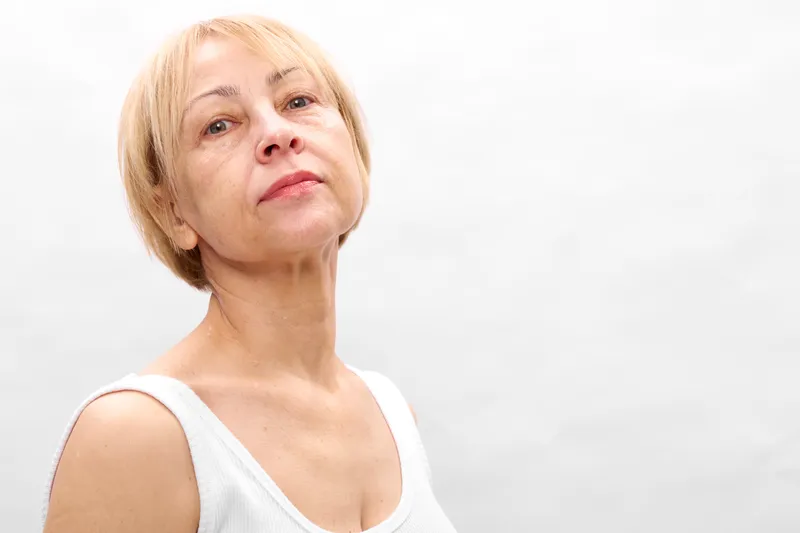 Elderly woman portrait in studio, gentle calm gaze upward, short light hair, soft natural skin tones, white background, relaxed posture, minimal composition