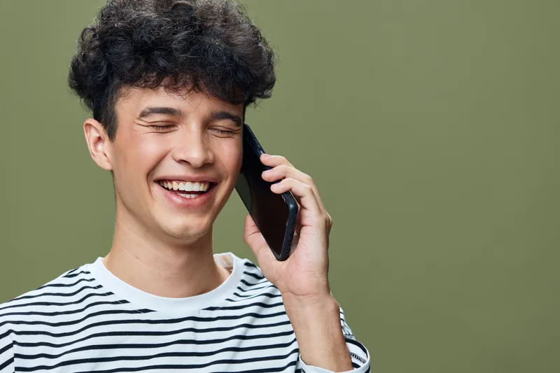 smiling man talking on smartphone with closed eyes wearing striped shirt against green background, happiness and communication concept.