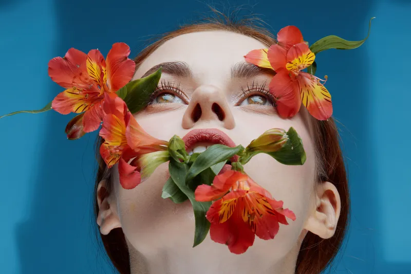 A serene female model with red hair surrounded by vibrant flowers, conveying emotions of tranquility and natural beauty against a blue background