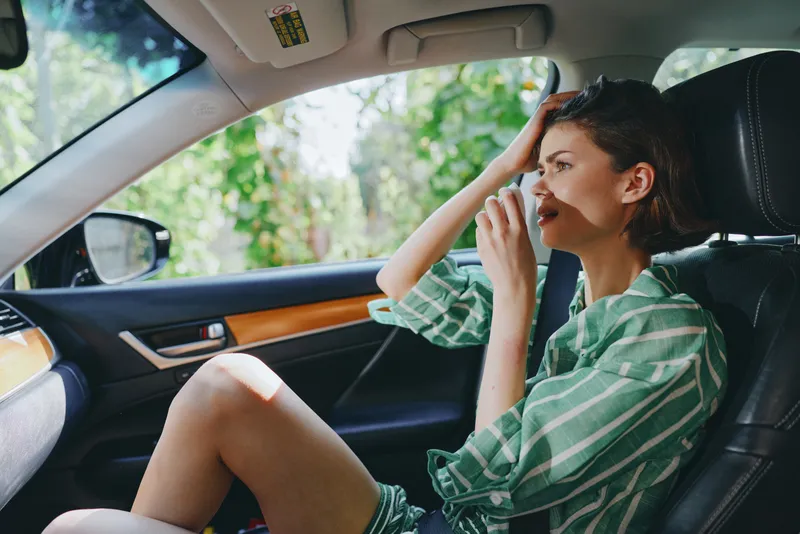 A woman sits in a car seat, talking on a mobile phone, wearing a striped shirt, relaxed posture, sunlight through the window, ready for a drive