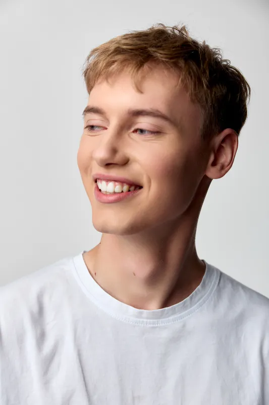Smiling young man wearing a white t shirt in a studio setting, relaxed pose and bright lighting, conveying casual confidence and a positive mood for lifestyle, wellness or fashion visuals