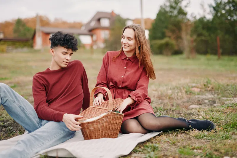 Young couple enjoying a simple outdoor picnic on a blanket, captured in an authentic, genuine moment of relaxed connection and everyday warmth in natural light.