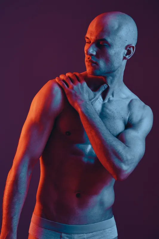 A striking image of a shirtless man highlighted in blue and red lighting, showcasing his muscular physique. The dramatic colors create an engaging visual impact.