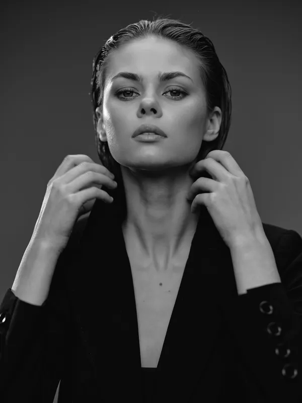 Black and white portrait of a confident woman with slicked-back hair in a dark blazer, expressing strength and elegance.