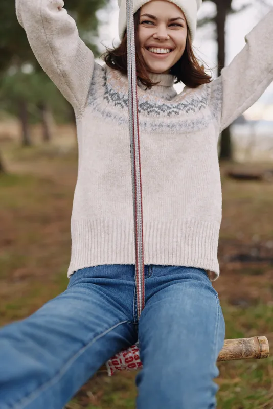 Woman on a swing in a park, smiling and enjoying a sunny day in a cozy knit sweater and jeans, capturing carefree outdoor leisure and simple everyday happiness