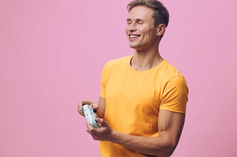 smiling man wearing yellow tshirt playing video game controller isolated on pink background casual lifestyle concept gaming entertainment