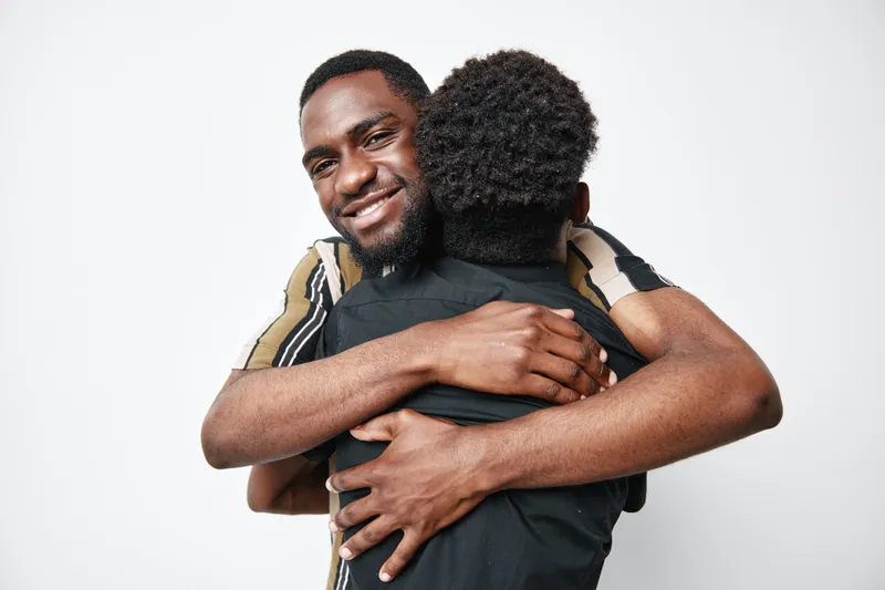 Two african american men hugging each other with smile and closed eyes for friendship, support and connection on white background. Dark skin, casual clothing and positive emotion.