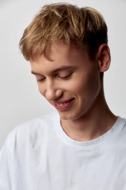Boy with a gentle smile in a white tshirt looking down, conveying quiet happiness in a casual mood, soft lighting and relaxed style for lifestyle and youth moments