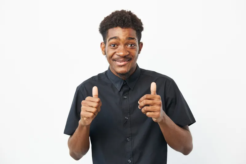Cheerful black man giving thumbs up, showcasing positivity and enthusiasm, dressed in a casual black shirt against a bright background.